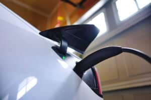 White EV electric car plugged and charging inside garage at home with green battery level indictor light. EV charger and energy saving concept
